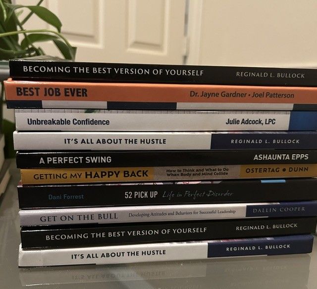 Stack of self-help books with motivational titles on a table, spines visible.