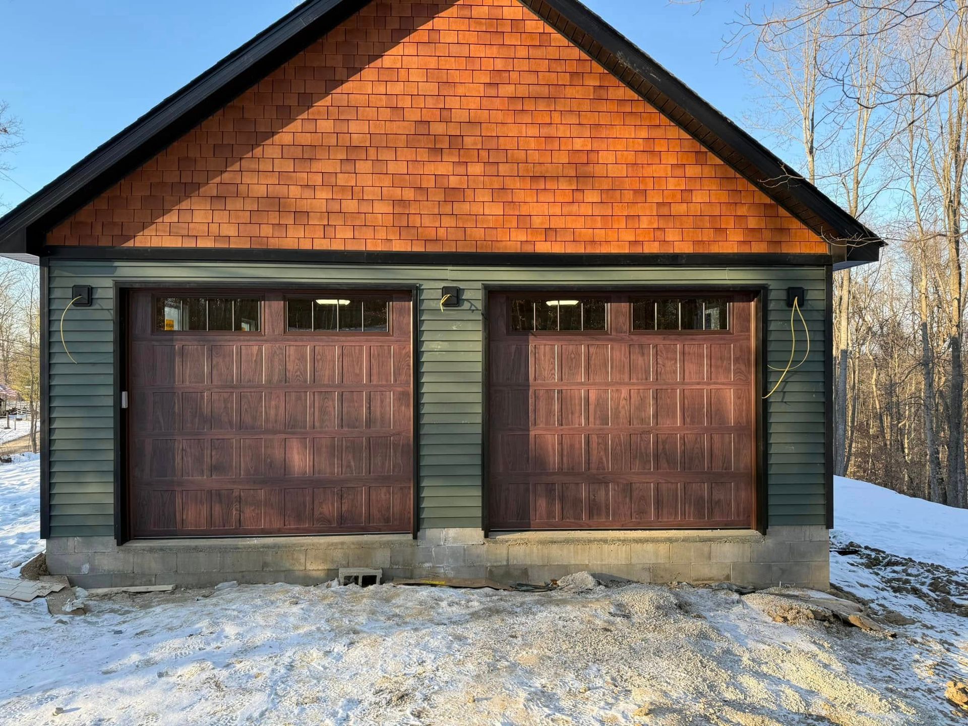 A garage with a red roof and green siding is covered in snow.