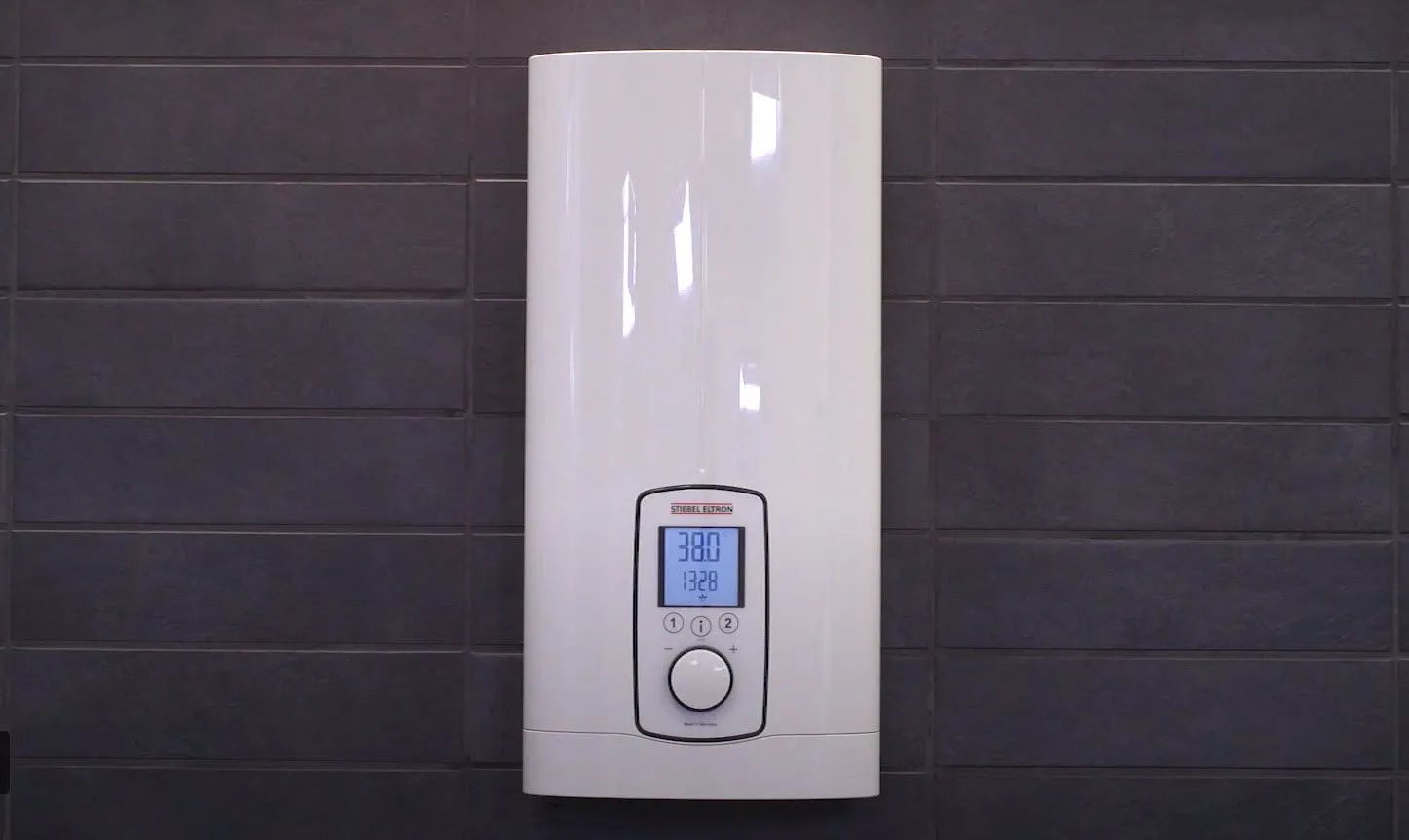 White water heater mounted on a dark gray tiled wall, with a digital display showing the temperature.