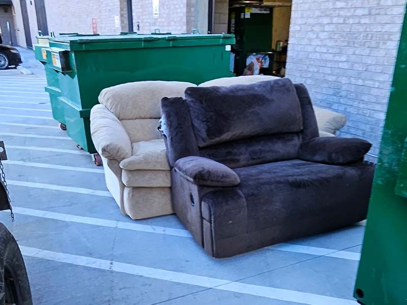 two recliner chairs are sitting next to a dumpster
