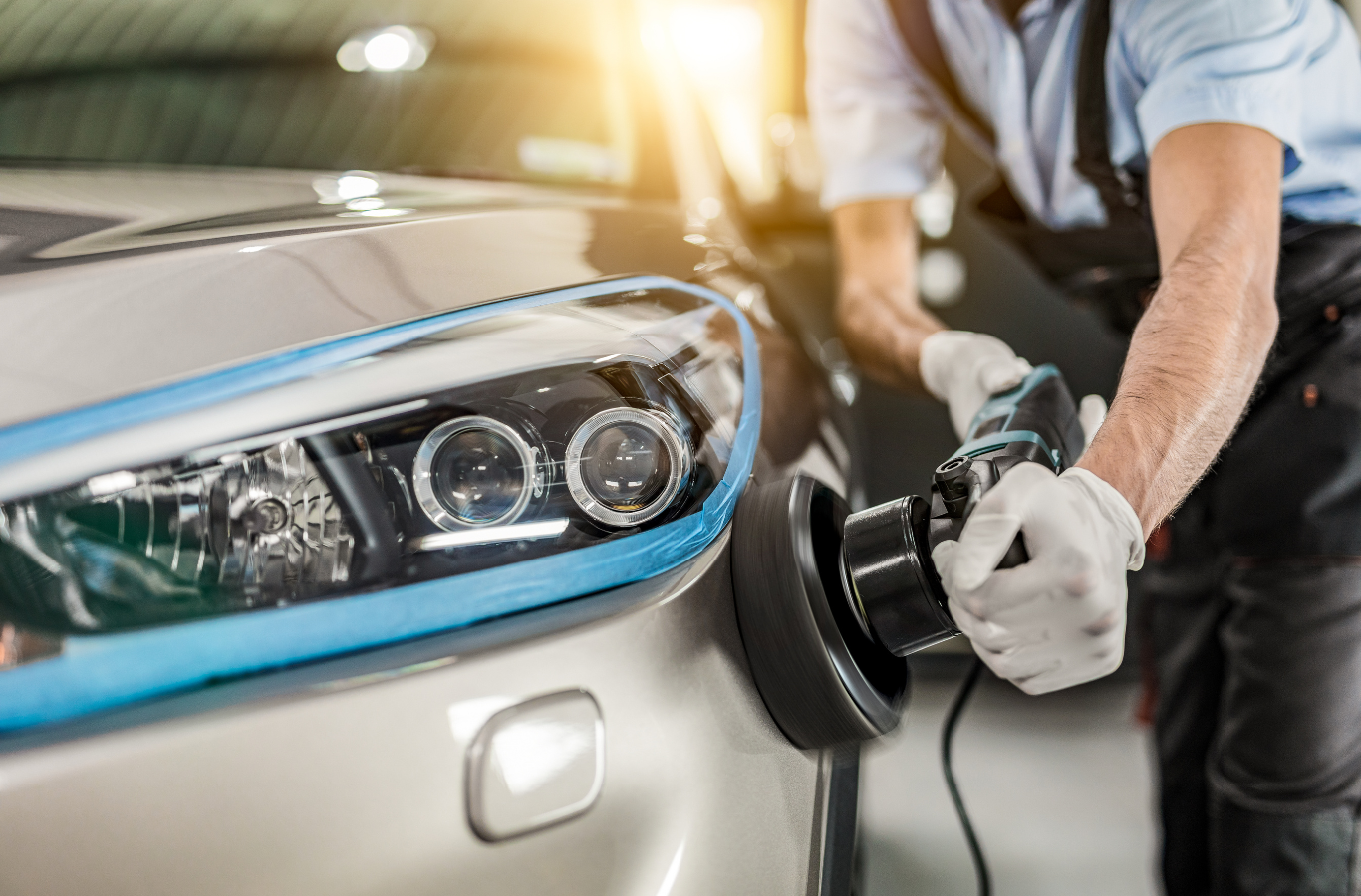 A man is polishing the headlights of a car in a garage.