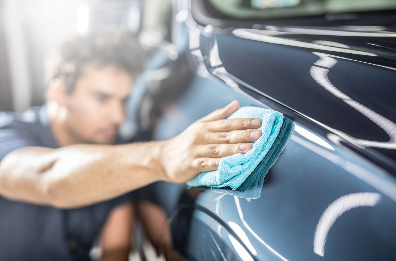 A man is cleaning a car with a cloth.