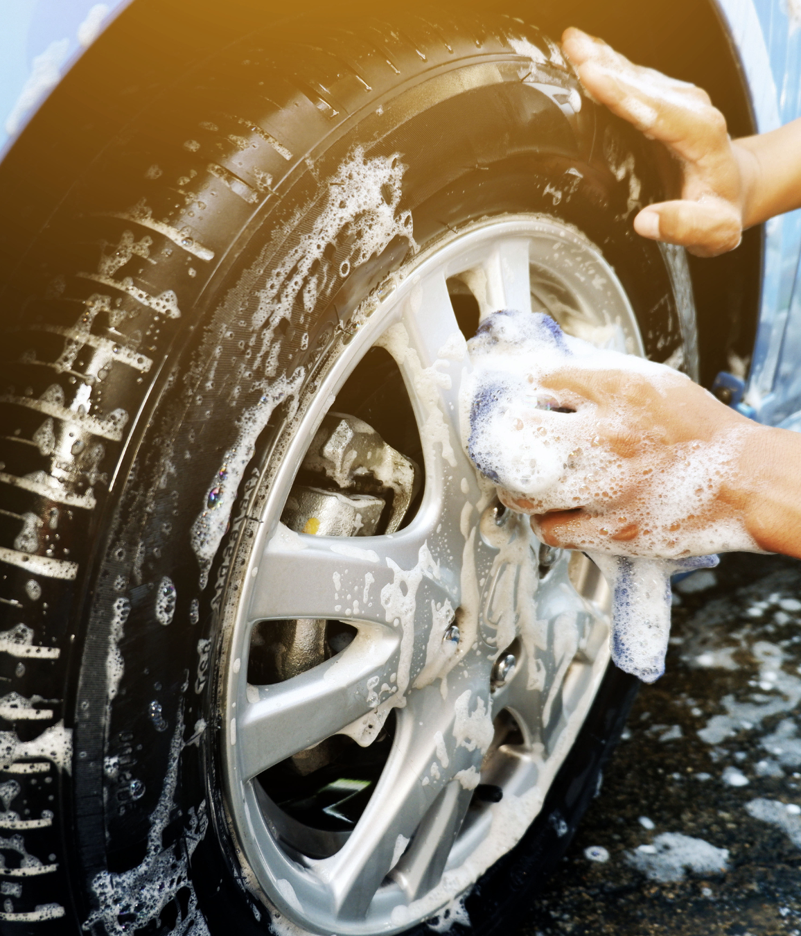 A person is washing a car wheel with soap and a towel.