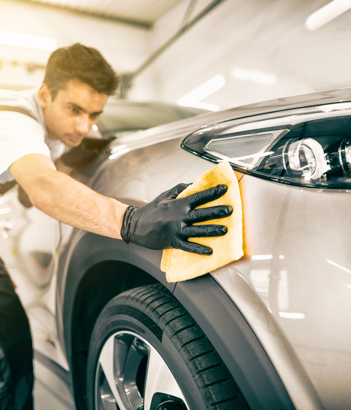 A man is cleaning a car with a yellow cloth.