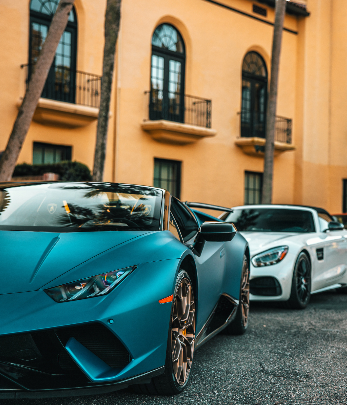 Two sports cars are parked in front of a yellow building.