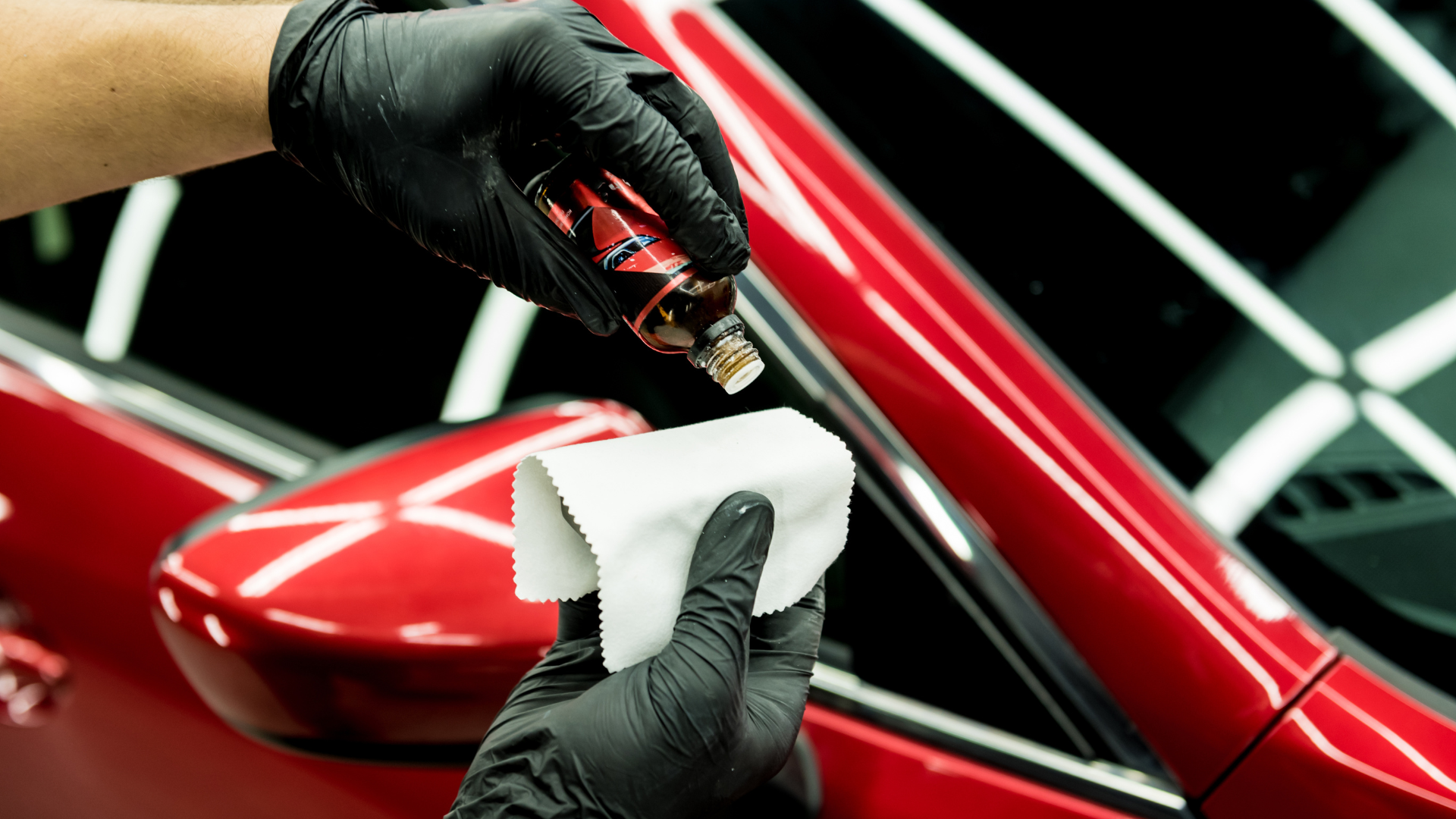 A person is applying a coating to a red car.