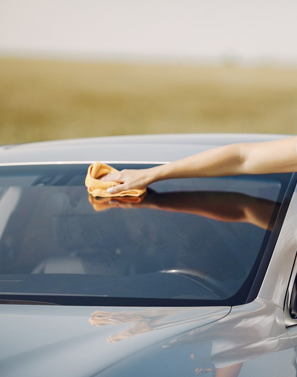 A woman is cleaning the windshield of a car with a cloth.