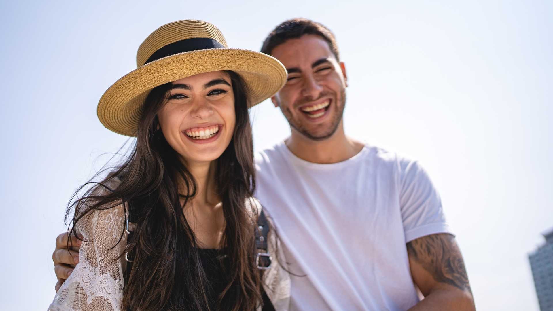 A man and a woman are standing next to each other and smiling . the woman is wearing a straw hat.