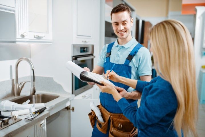 A smiling professional in workwear and a client reviewing a document in a kitchen.