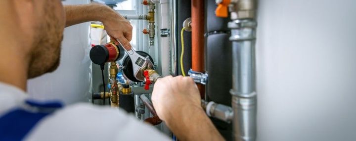 A technician using an adjustable wrench to repair plumbing pipes connected to a heating or cooling unit.