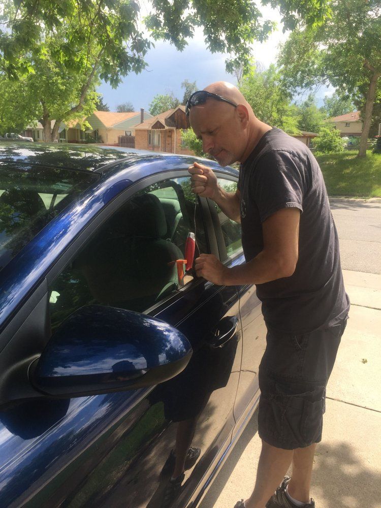 A man is standing next to a blue car on the side of the road.