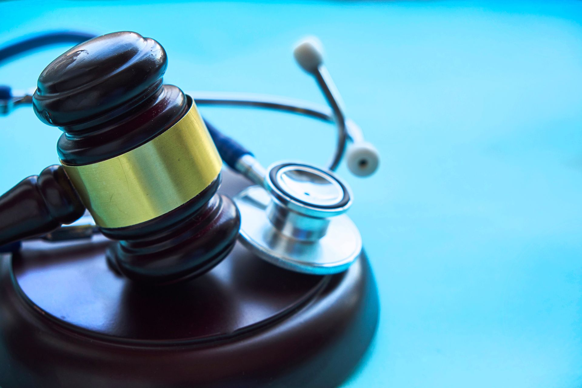 A wooden judge's gavel with a gold band resting next to a silver and black stethoscope on a light bl
