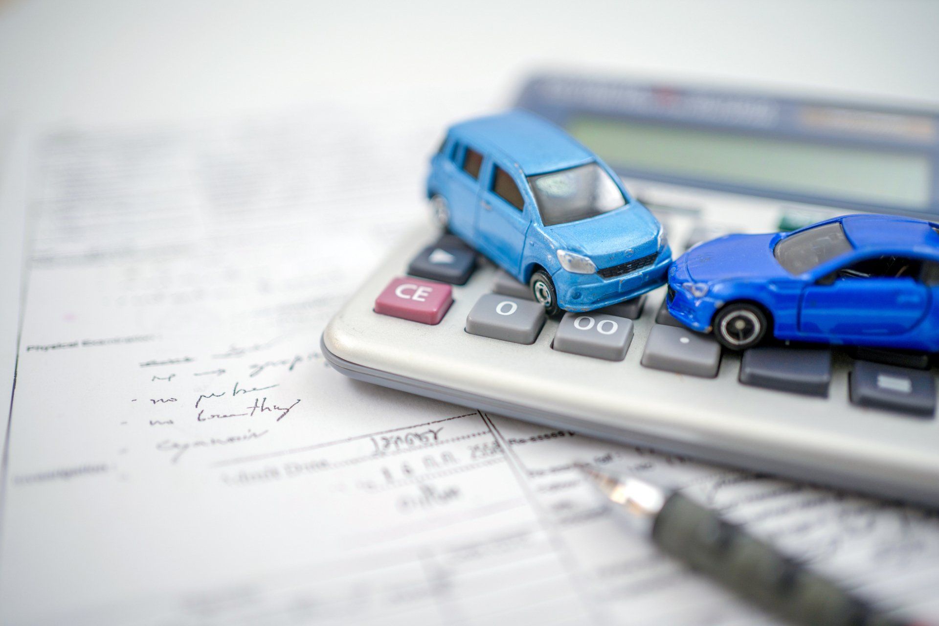 Two blue toy cars on a calculator atop a financial document with a pen.