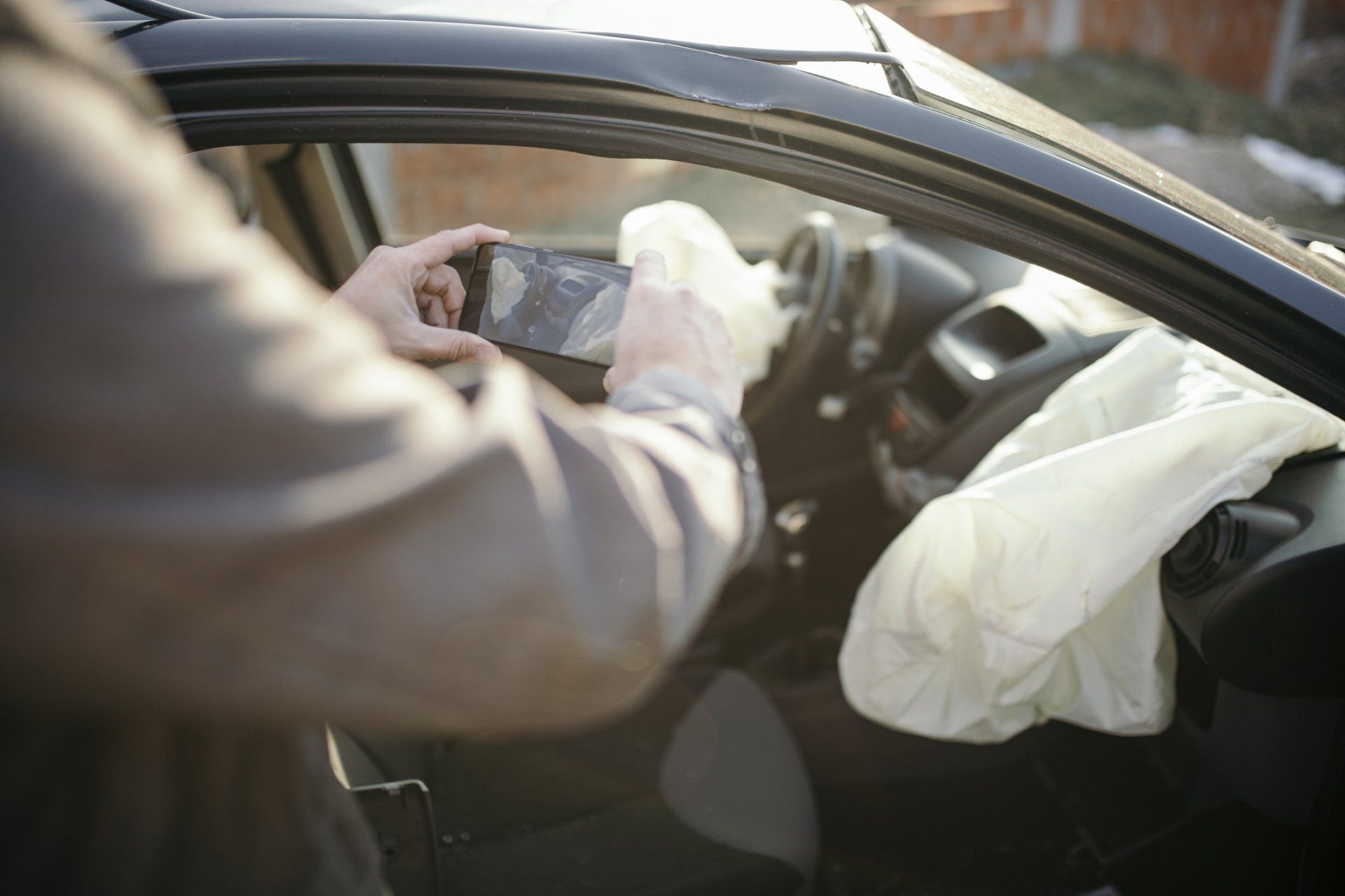 Person in a car taking a photo of deployed airbag and interior damage with a smartphone.