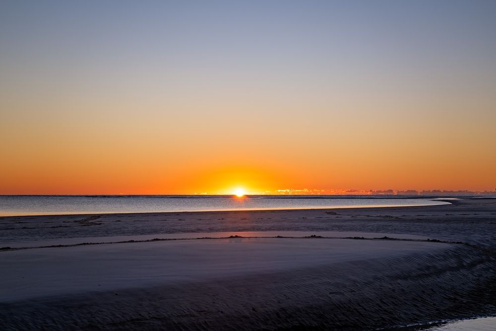 Sunset over water, orange sun near the horizon, reflecting in wet sand. — Serene Therapy with Lana In Paddington, NSW