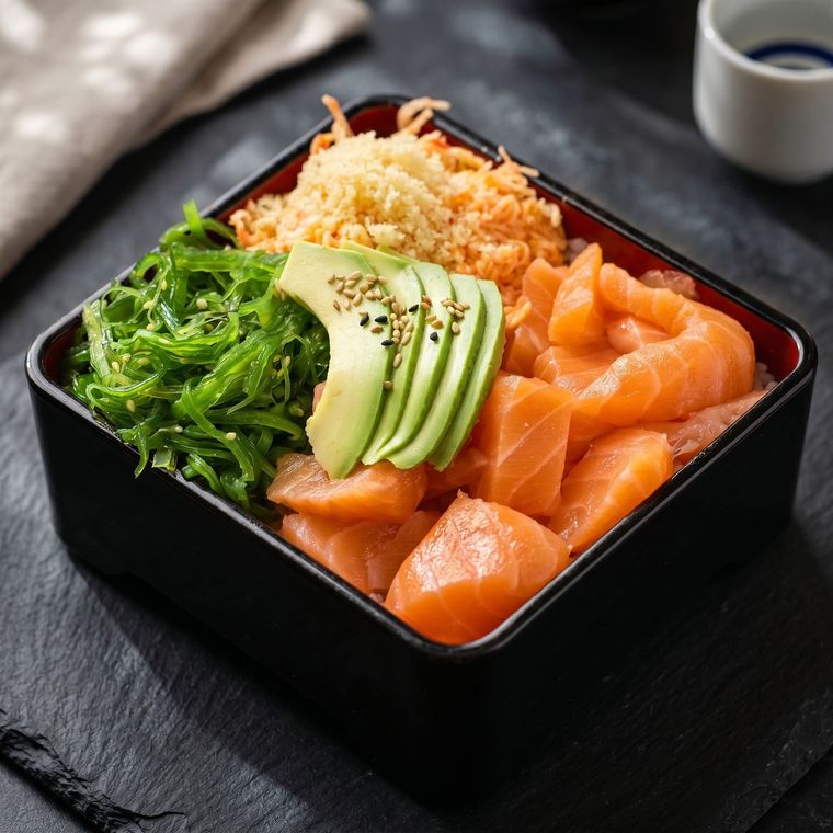 Sushi bowl with salmon sashimi, avocado slices, seaweed, and rice on a black tray