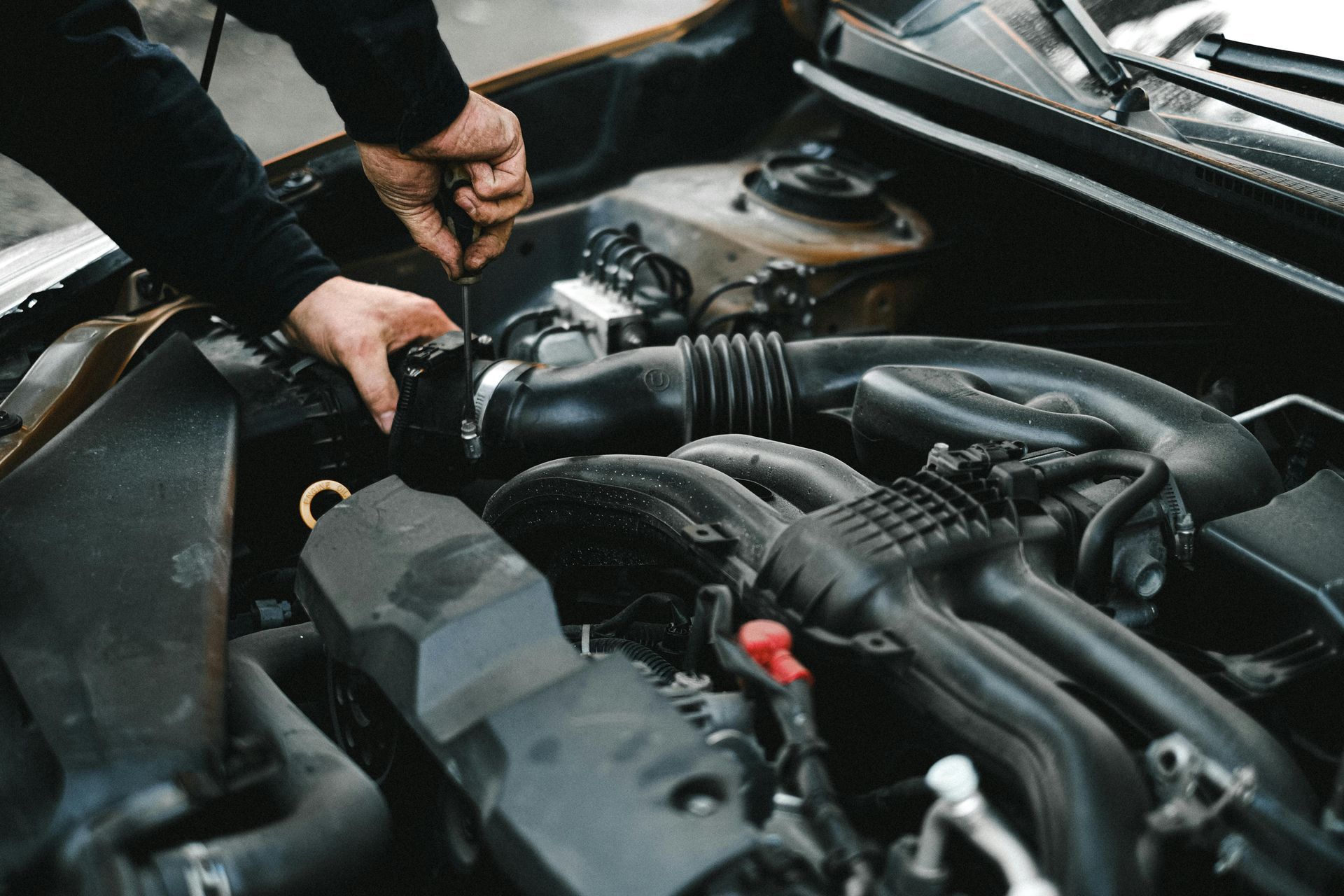 A person uses a tool to tighten a clamp on a black rubber hose inside a car engine bay.
