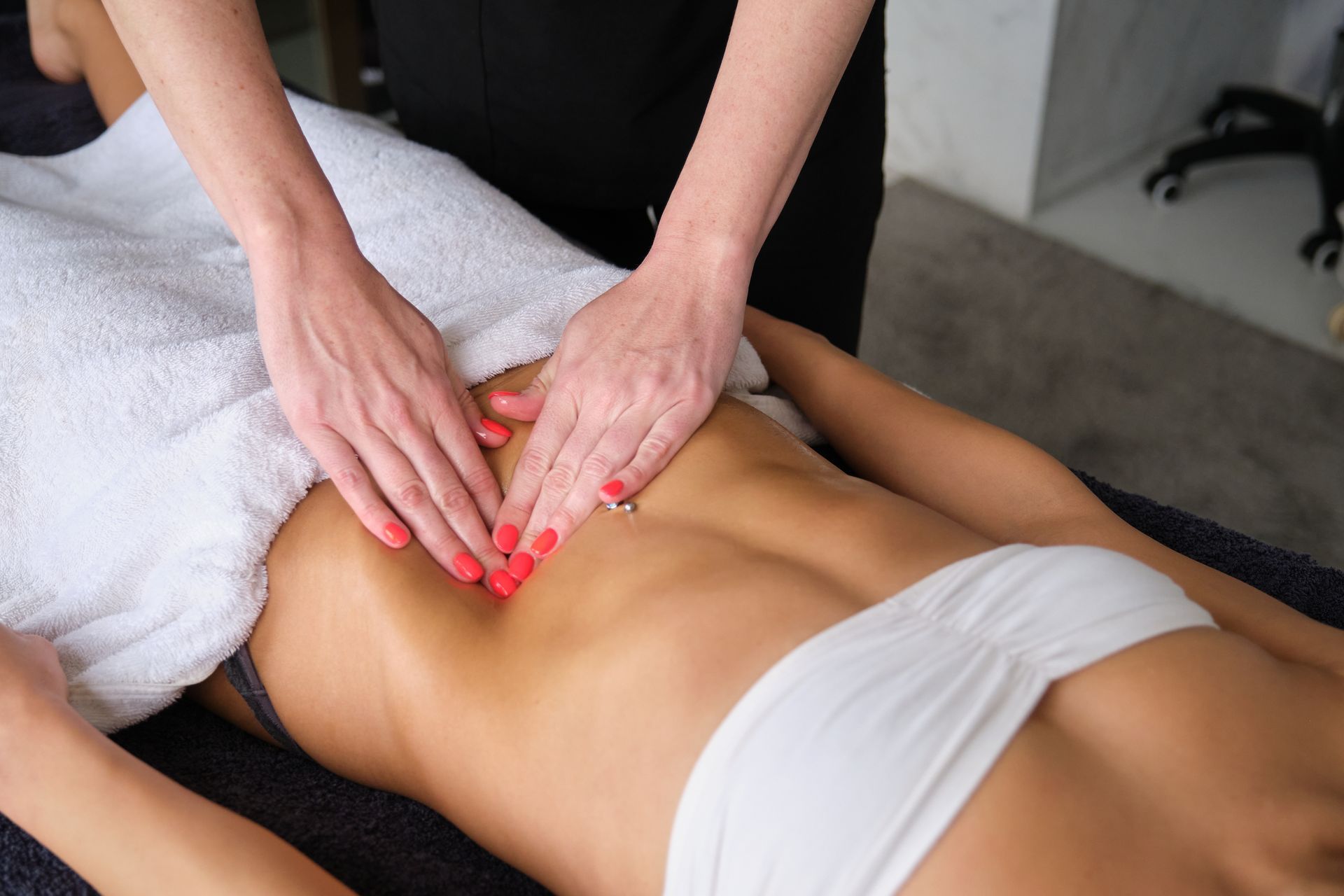 Hands massaging abdomen of person lying on a table, covered in a white towel, wearing a white top.