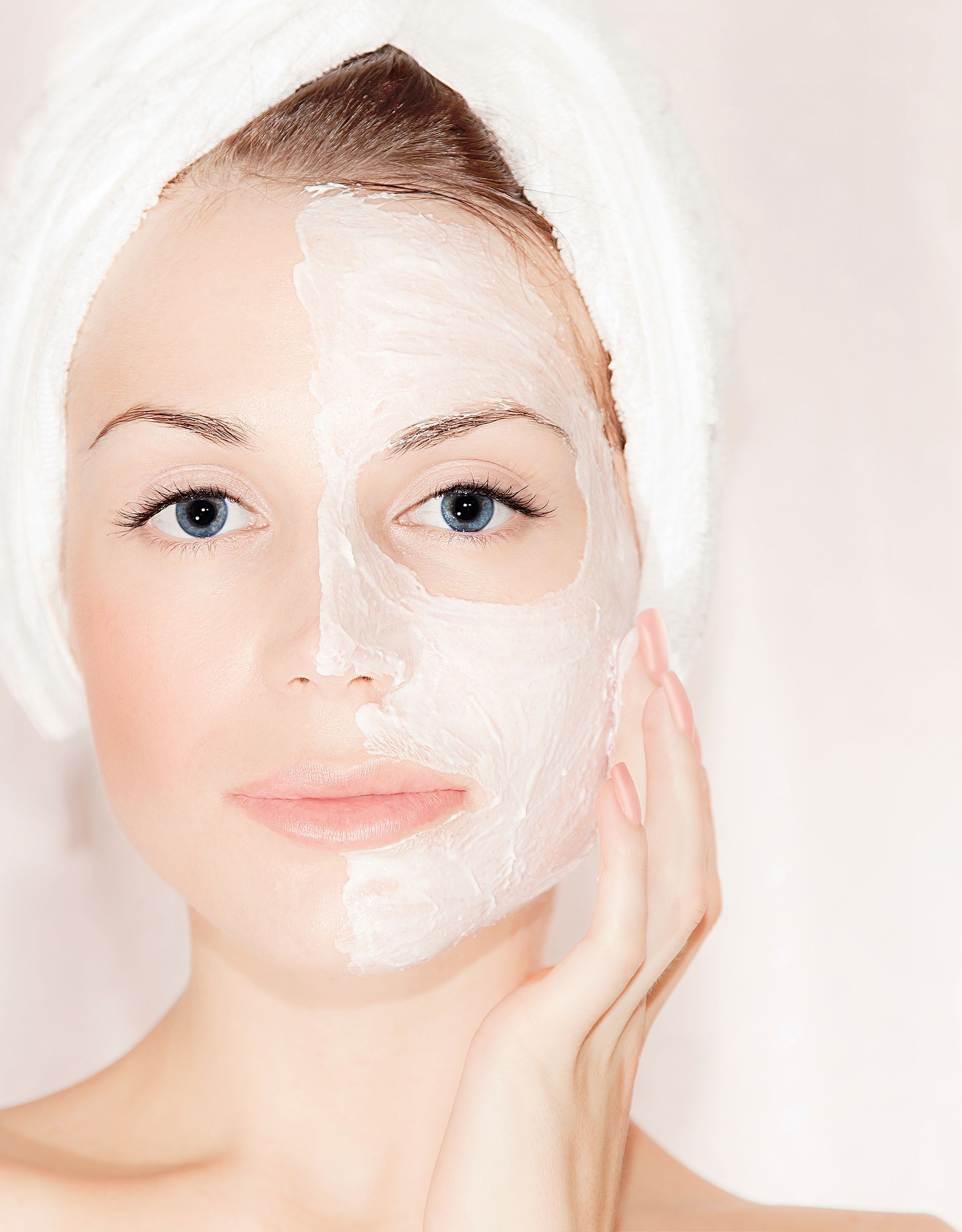 Woman with a white facial mask on half her face; looking at the camera.
