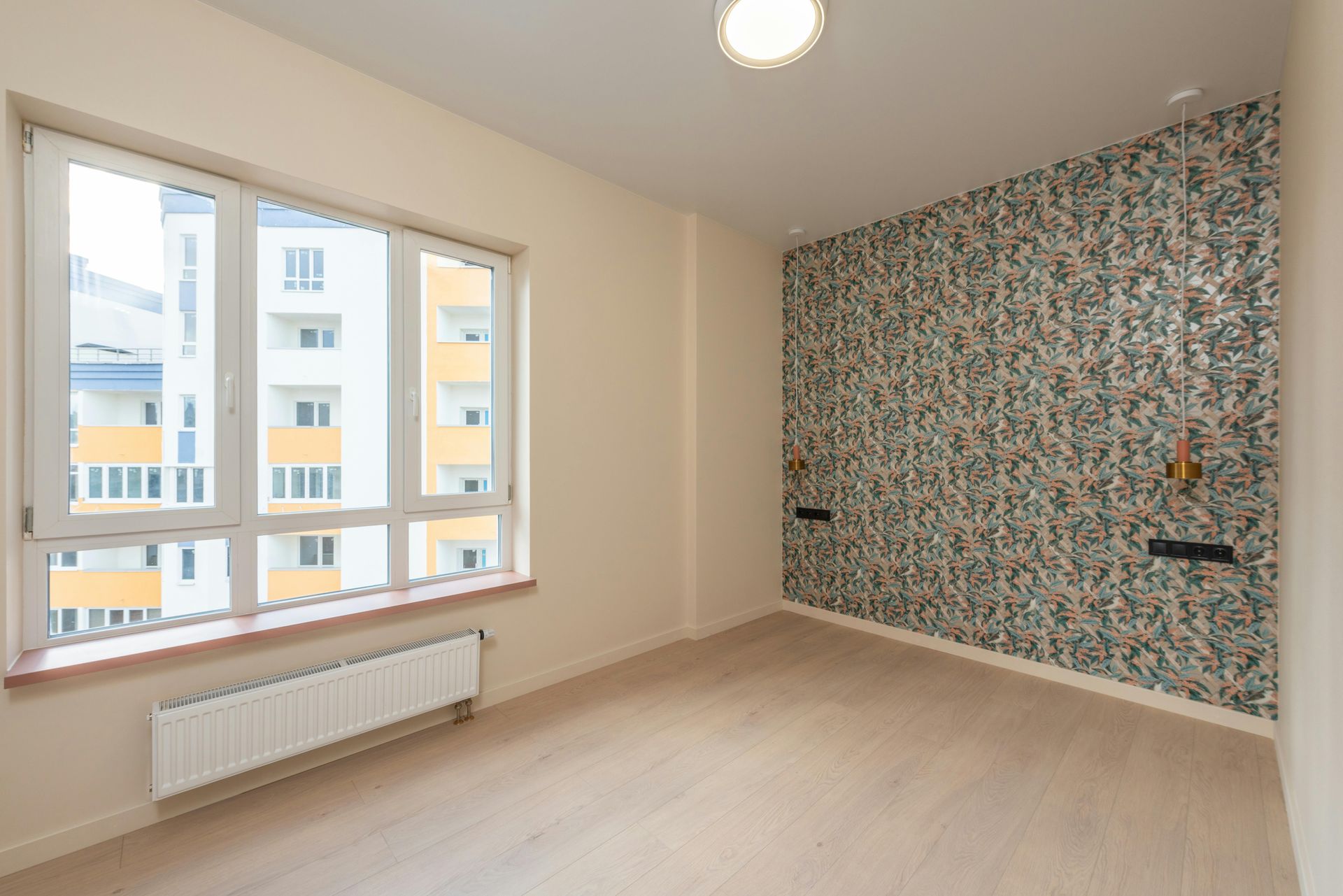 Empty bright room with window, radiator, and floral accent wall in a modern apartment