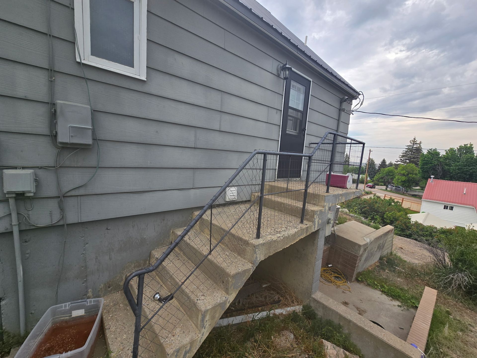 Gray house with exterior stairs leading to a door; metal railings; overcast sky.
