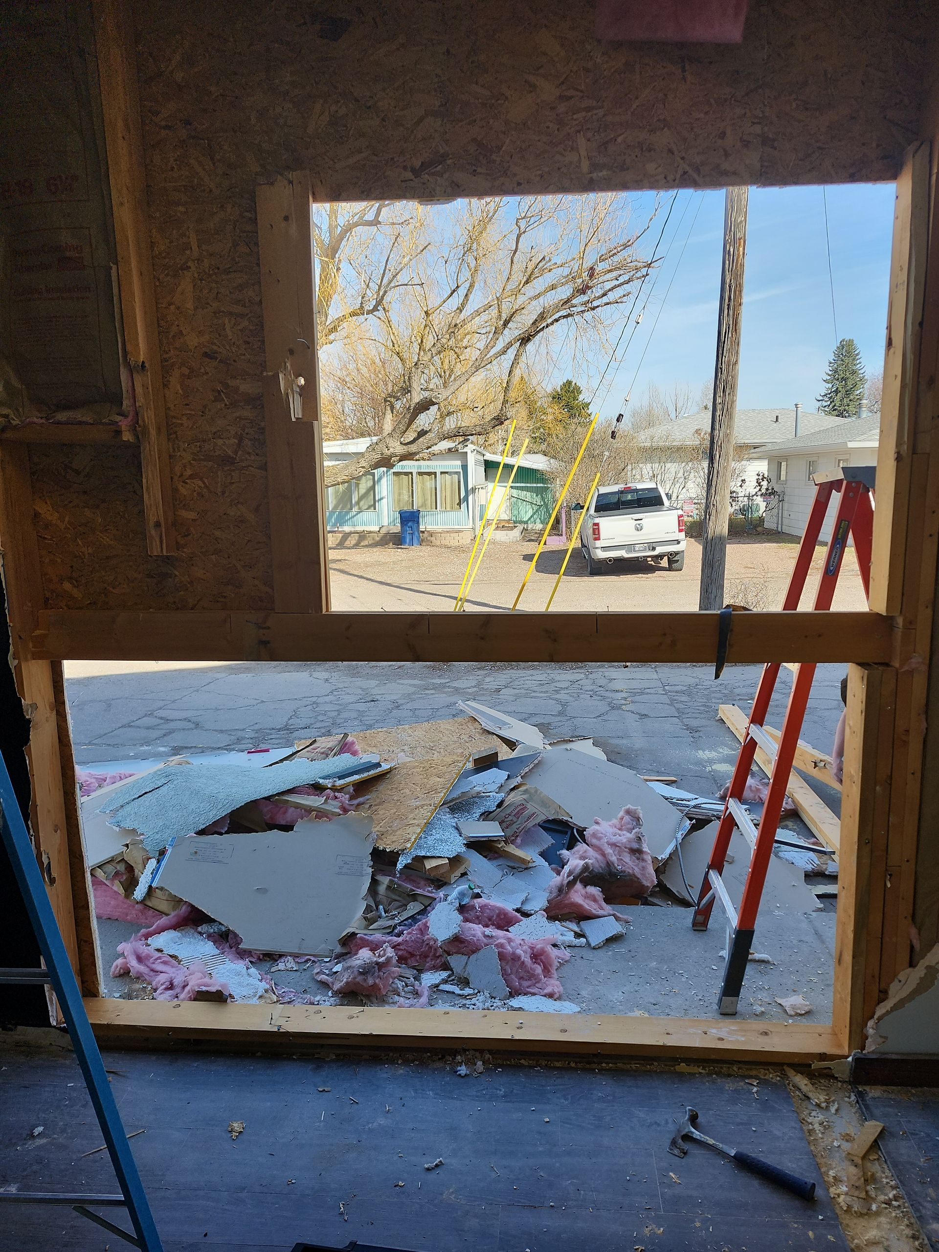 Interior view of a building under construction. A large opening shows debris and a street scene.