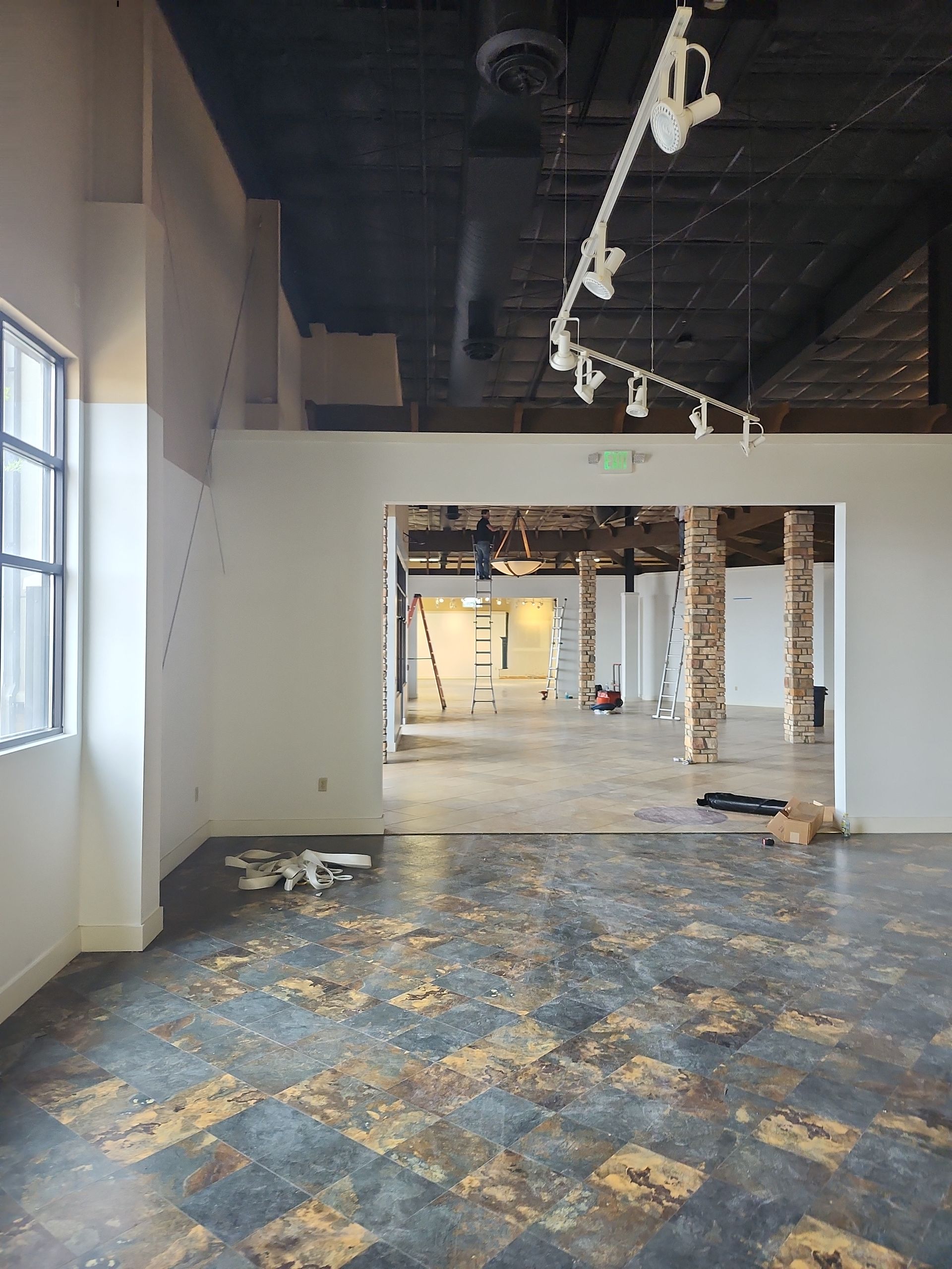 Empty interior space with worn floor, white walls, and exposed brick columns.