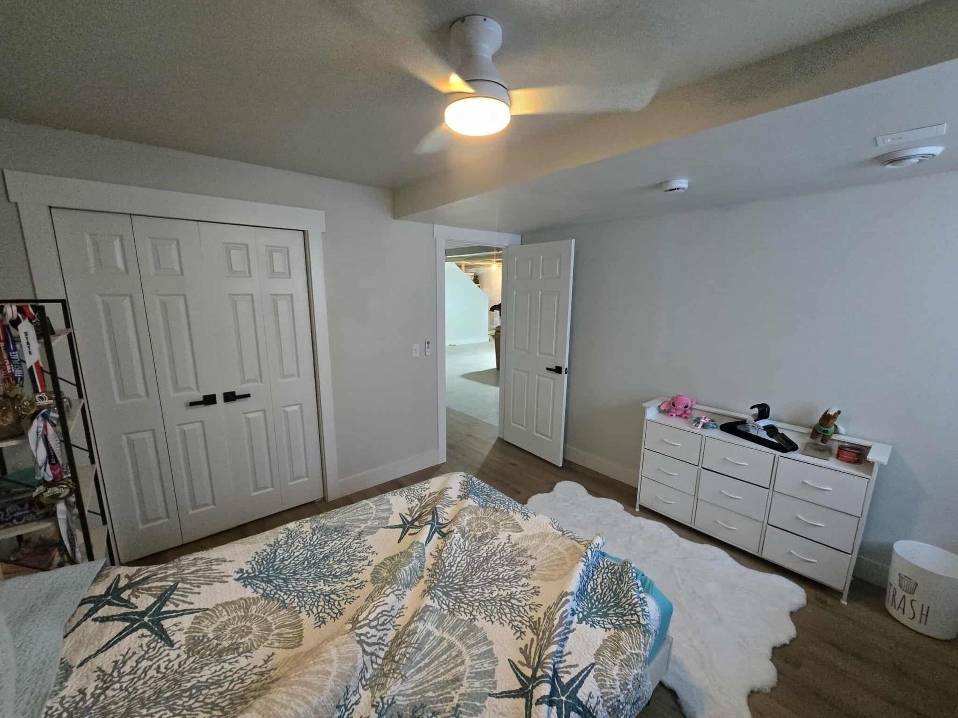 Bedroom with bed, white dresser, closet, door to hallway, and ceiling fan.