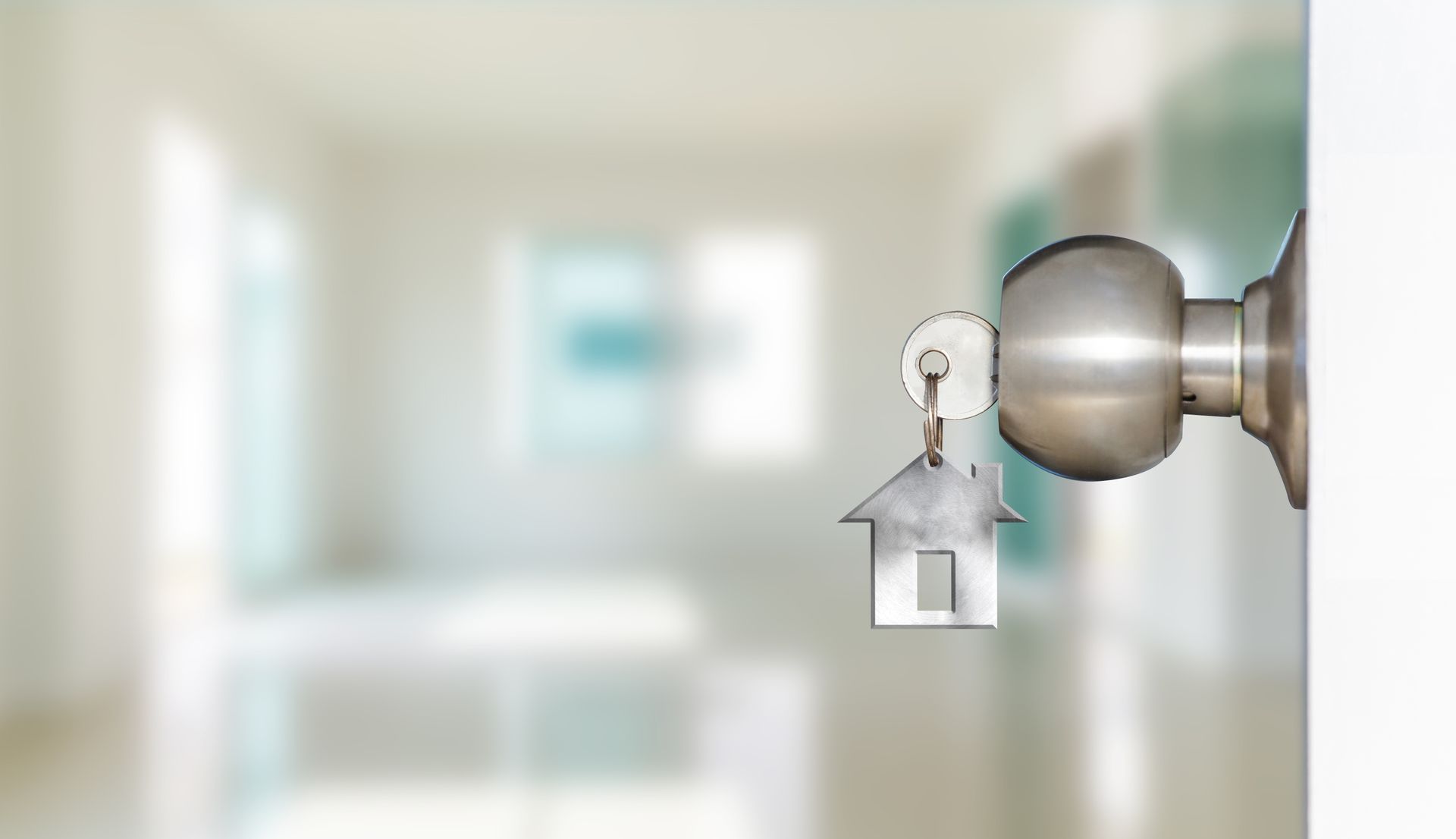 Clé insérée dans une poignée de porte avec un porte-clés en forme de maison ; arrière-plan intérieur flou.