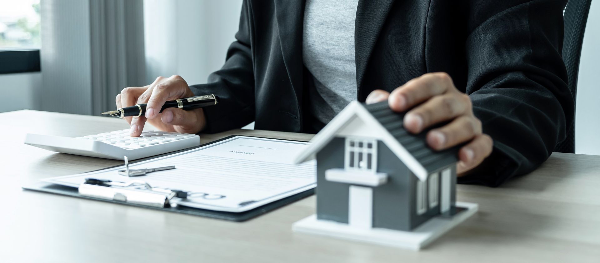 Une personne effectue des calculs sur une calculatrice à côté d'une maquette de maison posée sur un bureau.