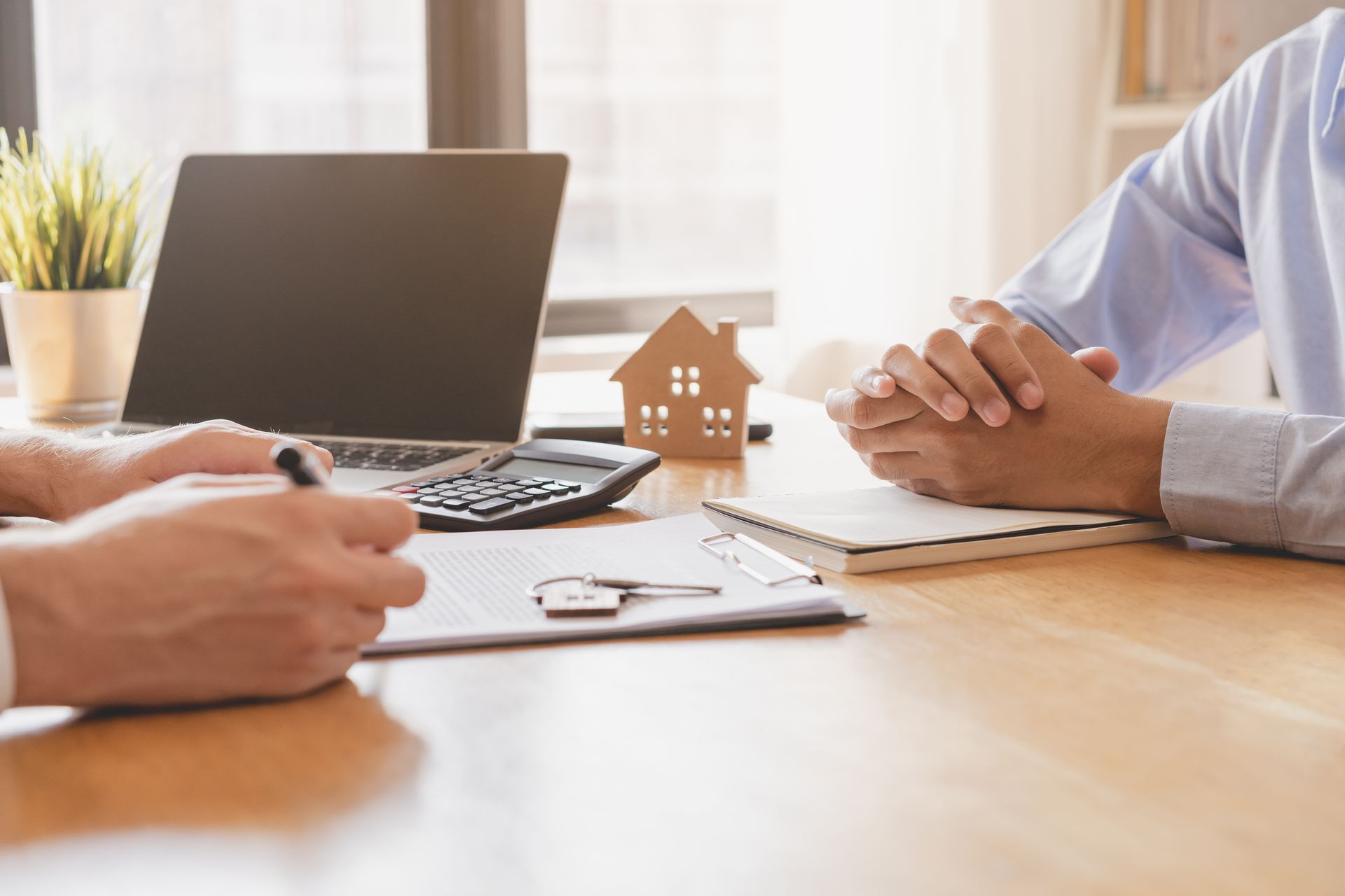 Personne signant un document avec les clés et une maquette de la maison sur le bureau.