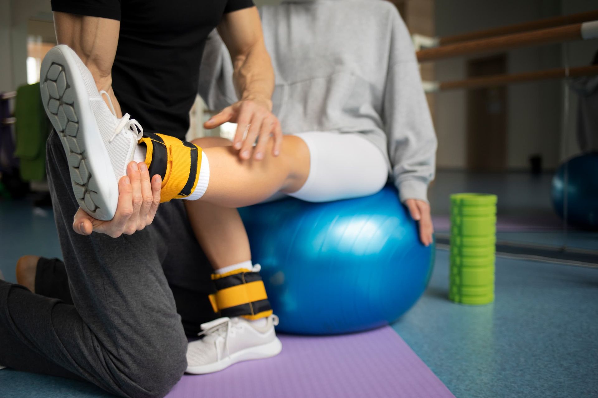 A man is helping a woman with her leg on a blue exercise ball.