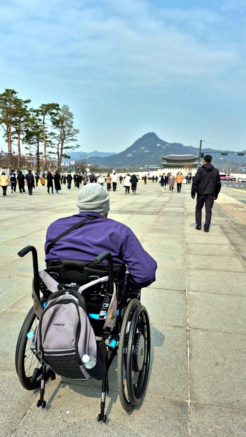 A man in a wheelchair is sitting on the sidewalk.