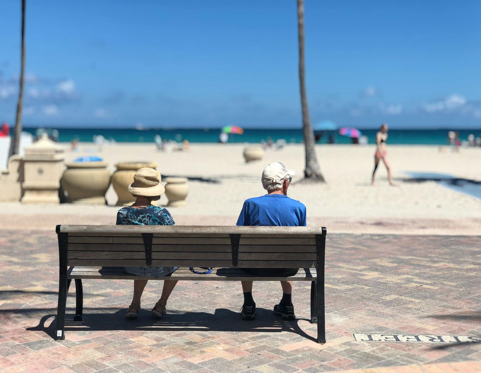 Two old people sitting on a bench at the beach.