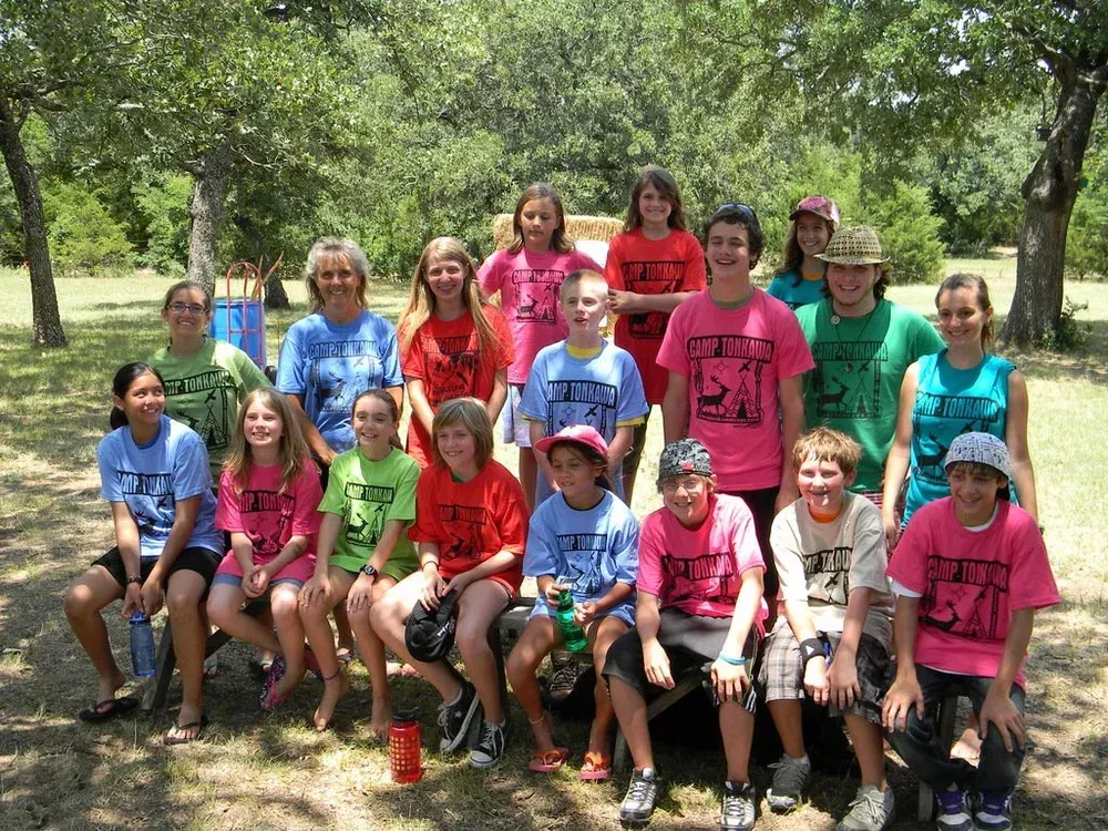 Group of people sitting and standing outdoors in a park, wearing colorful matching shirts.