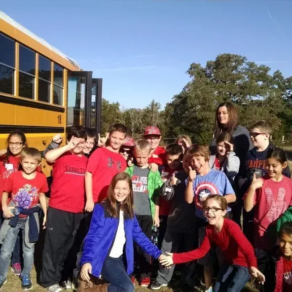 Group of children posing outdoors beside a yellow school bus on a sunny day