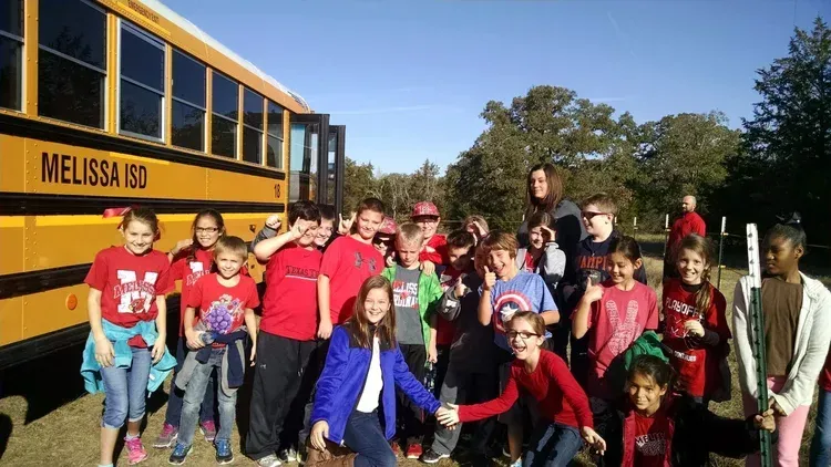 Group of students posing beside a yellow school bus on a sunny day