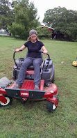 Person seated on a red mobility scooter on a grassy field with trees in the background