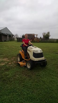 Person riding a yellow lawn tractor on a grassy yard under a cloudy sky