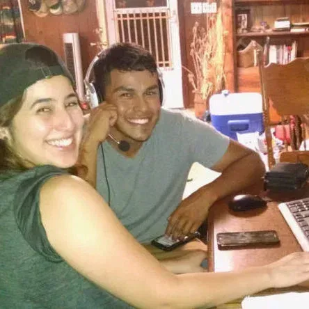 Two smiling coworkers at a desk, one wearing a headset, in a warm office setting