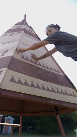 Person painting a large triangular structure with brown and white geometric patterns outdoors