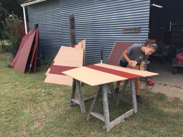 Person assembling a red-and-beige wooden panel on sawhorses outside a shed