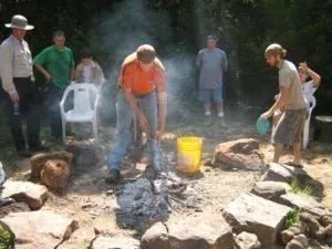 People standing around a smoky outdoor fire pit with rocks and a yellow bucket