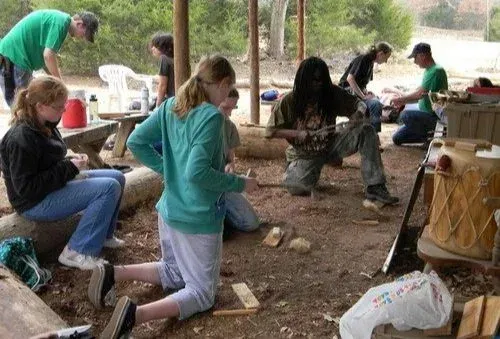 People gathered around a wooden structure in a wooded outdoor area, examining it together.