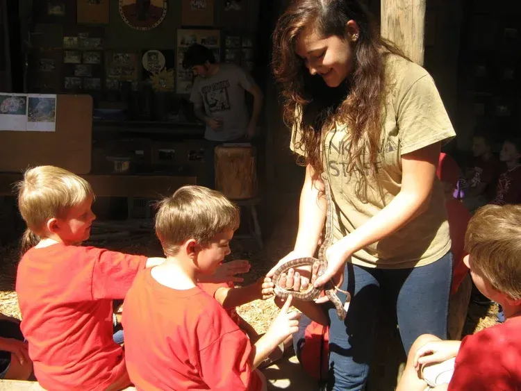 Woman handing an object to children outdoors in front of a building
