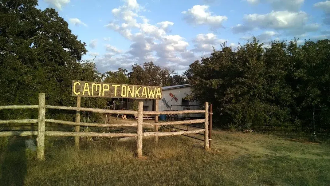 Wooden fence and yellow “CAMP TOWN” sign in a grassy field under a cloudy sky
