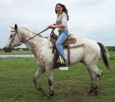 Woman riding a white horse in a grassy field under an overcast sky