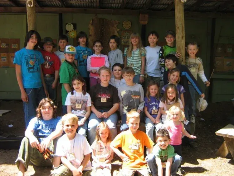 Group of people posing in front of a rustic building, some seated and some standing, in bright casual clothes