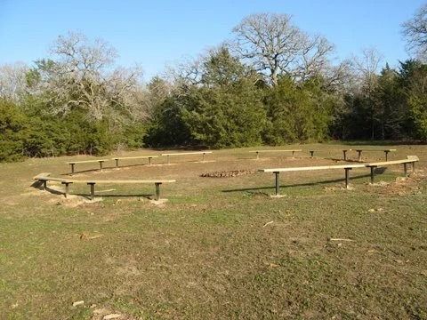 Grassy outdoor arena with low wooden rails, surrounded by trees under a clear sky
