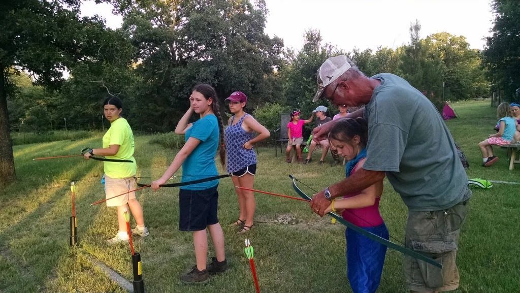 People watering plants in a garden at sunset, with a man helping a child nearby.
